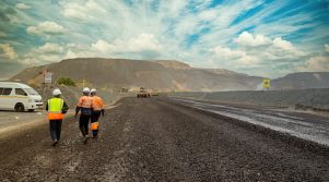 Few African workers walking on a dirt road at open pit diamond mine, heavy machinery in the background